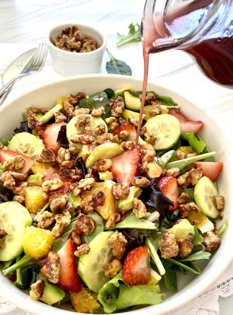 pouring berry vinaigrette on strawberry walnut salad